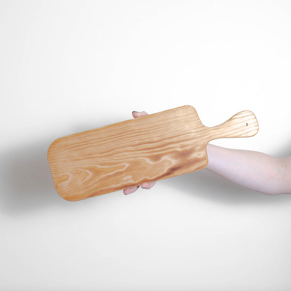 A person delicately holding a Bespoke 77 Small Pine Serving Board/Paddle.