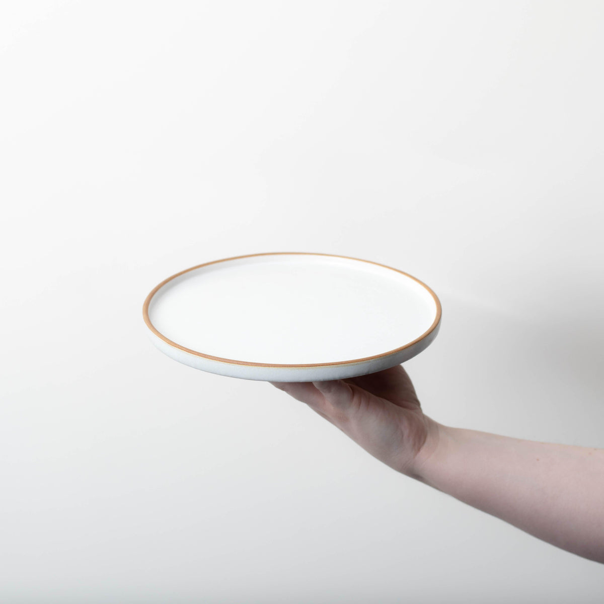 A person holding a Bespoke 77 Matte White With Rye Edge 20cm Flat Plate with a gold trim.